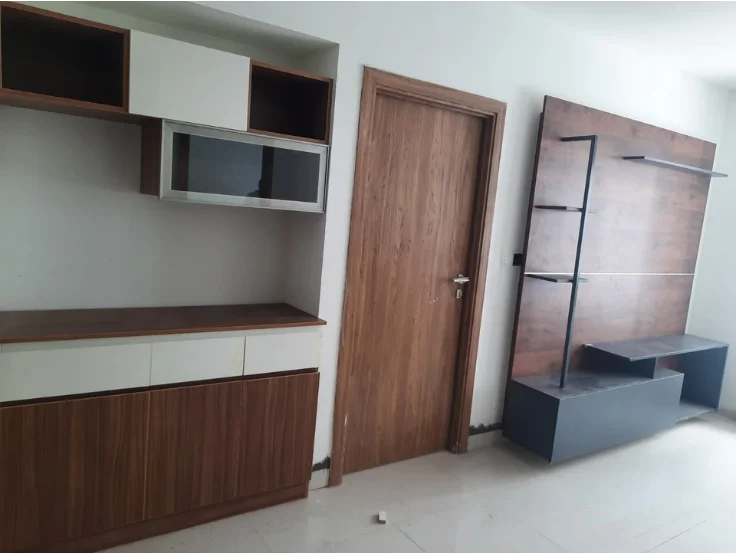 A room with an empty wooden cabinet on the left and bookshelf on the right, next to a closed door.