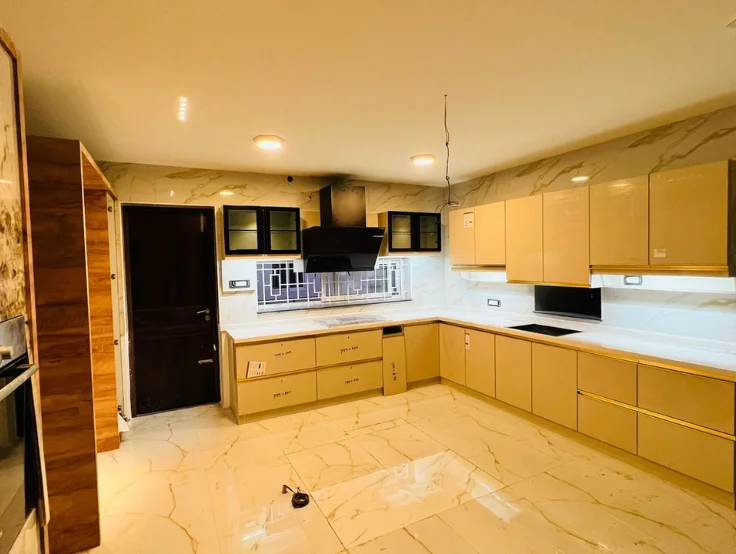 A modern kitchen interior with beige cabinets, marble walls, and beautiful shiny floor tiles.