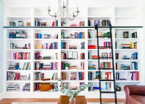 A wooden bookcase filled with books, featuring a ladder for quick access to the upper shelves.