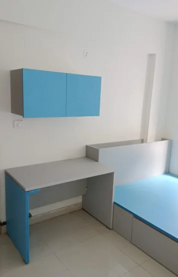 A modern room featuring blue and white furniture with a bed, stylish desk, and spacious wall cabinets.