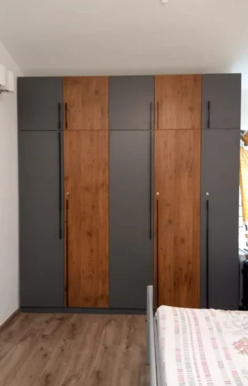 A modern wardrobe featuring gray panels & wooden doors, adding a contrast to the bedroom decor.