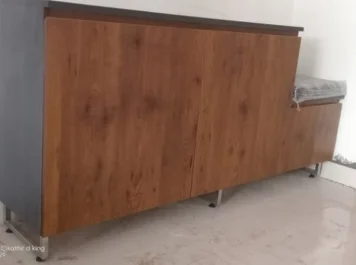 A wooden cabinet with sleek closed doors stands in a room, next to a covered object on the right side.