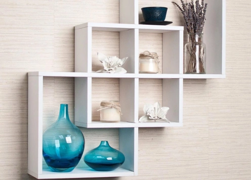 White geometric wall shelves display decorative blue vases, candles & flowers, adding a stylish touch.