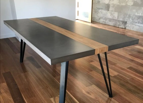 Modern table with a concrete top, wooden strip inlay, and black metal legs on a wooden floor.