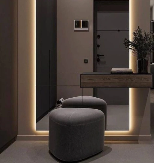 A trendy foyer with a full-length mirror illuminated by LED lights, a vanity table & upholstered stools.