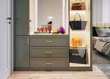 A modern dressing area with a vanity, drawers & a glass-paneled closet displays handbags and accessories.