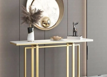 Modern console table with golden accents, decorative items, and round mirror against a grey wall.