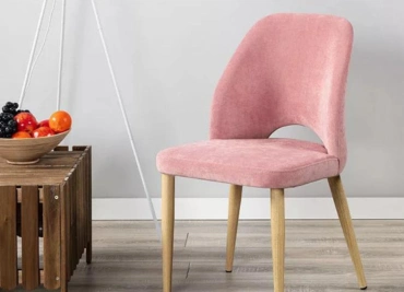 Stylish pink accent chair with wooden legs next to a fruit bowl, adding a charming touch to any room