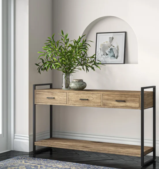A modern console table with storage drawers, a potted plant, and framed artwork in a bright room.