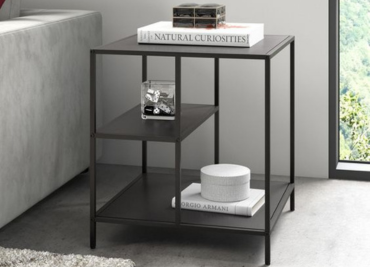 Modern black metal side table with two shelves holding books and decorative items, by a window.